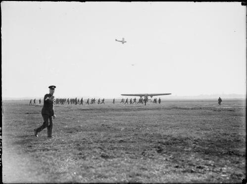Policemen running to surround a triple engined monoplane, possibly the Southern Cross, as it taxis across an airfield, Australia, ca. 1930 [picture] / E.W. Searle