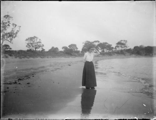 Woman standing on a beach beside the sea, Australia, ca. 1900 [picture] / E.W. Searle