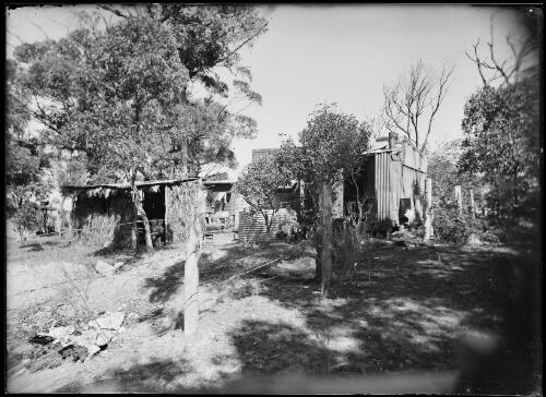 Seated women with children behind a group of outbuildings, Australia, ca. 1945 [picture] / E.W. Searle