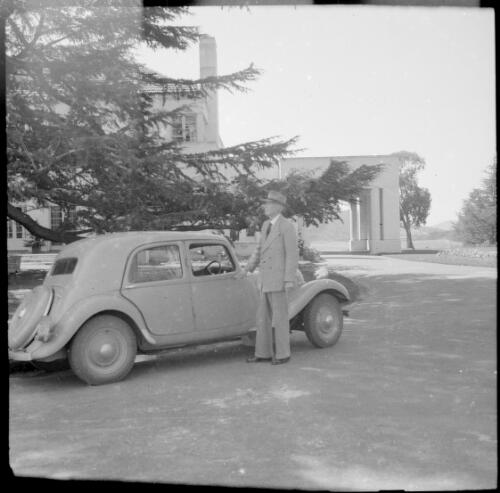 E.W. Searle, wearing a hat, beside his Citroen, outside the entrance to the Governor-General's residence, Yarralumla, Canberra, ca. 1949 [picture] / E.W. Searle