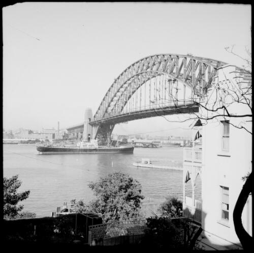 Cargo ship passing under the Sydney Harbour Bridge, Kirribilli, Sydney Harbour, ca. 1935 [picture] / E.W. Searle