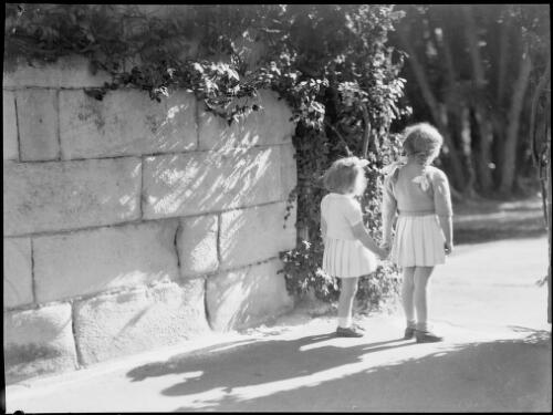 Two young girls beside a stone wall, Royal Botanic Gardens, Sydney, ca. 1935 [picture] / E.W. Searle