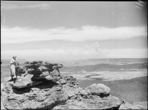 Mrs Searle standing on a rock ledge overlooking a plain, Australia, ca. 1945 [picture] / E.W. Searle