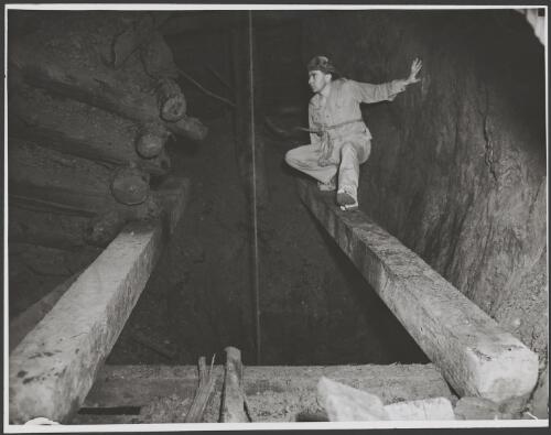 Man, squatting on a beam, beside a taut rope passing down a mineshaft, Australia, ca. 1935 [picture] / E.W. Searle