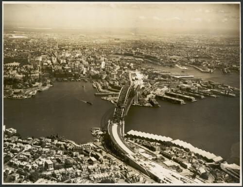 Aerial view of an incomplete Sydney Harbour Bridge from the north with Circular Quay to the side, Sydney Harbour, 1931 [picture] / E.W. Searle