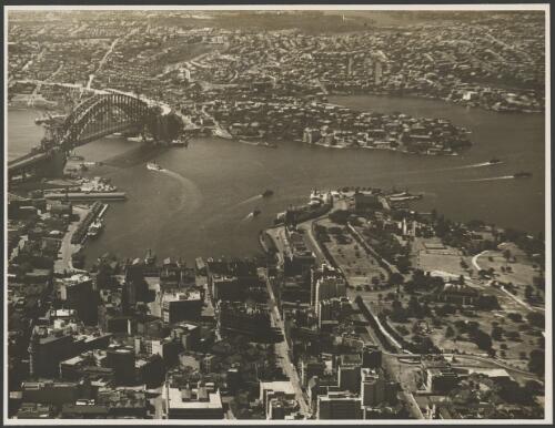 Aerial view of an incomplete Sydney Harbour Bridge with Circular Quay in the foreground, Sydney Harbour, 1931, 1 [picture] / E.W. Searle