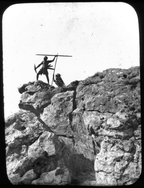 Two Aborigines with spears on rock ledge [transparency] / E.W. Searle
