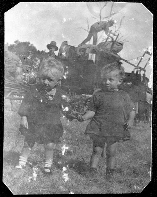 Two young children holding hands, men unloading a cart in backgound, during the St. Leon and Sole Brothers Circus and Zoo tour of Australia, ca. 1923 [picture]