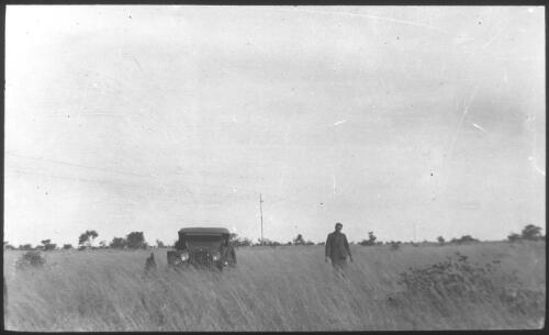 [Man standing beside car in long grass] [transparency] : a deputation lantern slide of the AIM [Australian Inland Mission] Head Office, 1926-1940 / [John Flynn?]