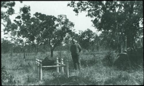 Minister standing near the grave of Aeneas James Gunn, the Maluka, Elsey Cemetery, Northern Territory [transparency] : taken on a survey trip undertaken by Rev. J.A. Barber and Dr. George Simpson for the Flying Doctor Scheme