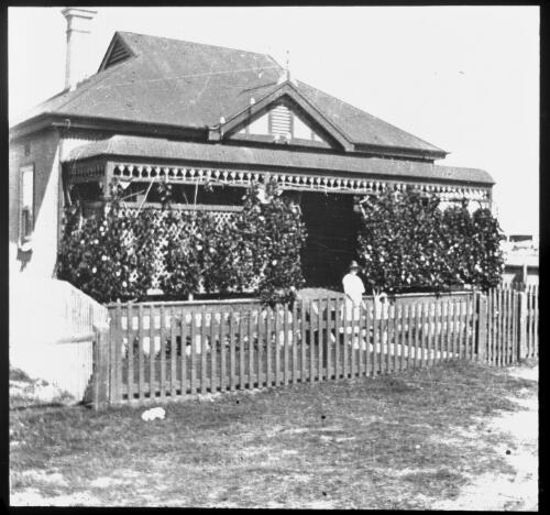 Unidentified woman with a hat standing in the front yard of an ivy-covered house [picture] : Fred McKay Cape York Peninsula and West Queensland Patrol 1938-1940 / [Fred McKay]