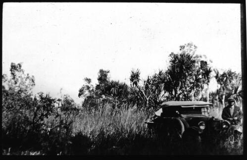 Man standing beside car in scrub [transparency] : a deputation lantern slide of the AIM [Australian Inland Mission] Head Office, 1926-1940 / [John Flynn?]