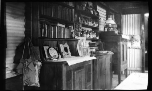 Interior of home with cabinets and shelves laden with books, jars and family portraits [transparency] : a deputation lantern slide of the AIM [Australian Inland Mission] Head Office, 1926-1940 / [John Flynn?]