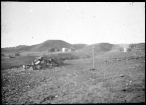 Man with pumps?, unidentified buildings on a hilly landscape [transparency] : lantern slide used by Rev. F.H. Paterson, north South Australia / [John Flynn?]