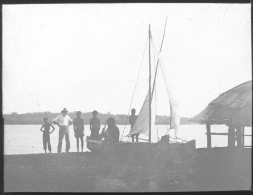 Unidentified man wearing hat standing next to group of Aboriginal men, small sailing boat in foreground [transparency] : miscellaneous glass slide / [John Flynn?]