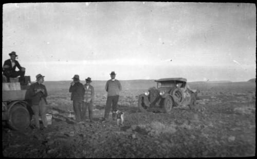 Group of men standing next to a car having a smoko in West of Port Augusta [transparency] : taken on a survey trip undertaken in 1927 by Rev. J.A. Barber and Dr. George Simpson for the Flying Doctor Scheme