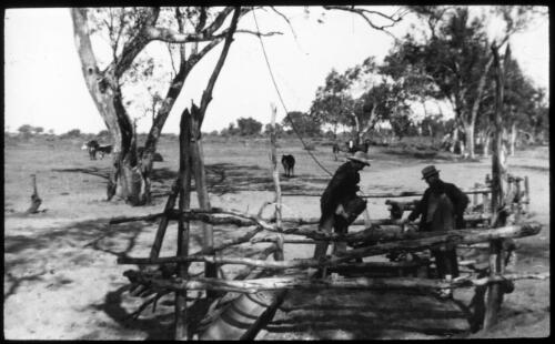 Unidentified men drawing water from a whip well in Hermannsburg, Northern Territory [transparency] : taken on a survey trip undertaken in 1927 by Rev. J.A. Barber and Dr. George Simpson for the Flying Doctor Scheme