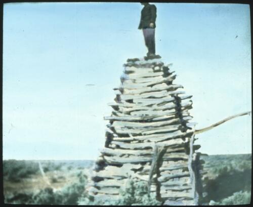Unidentified man standing on top of a tower built from timber [transparency] : taken on a survey trip undertaken in 1927 by Rev. J.A. Barber and Dr. George Simpson for the Flying Doctor Scheme
