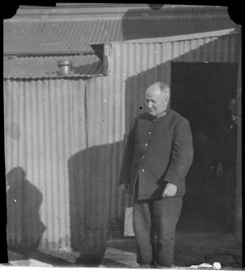 Uniformed man outside a corrugated iron building [transparency] : a deputation slide of the AIM [Australian Inland Mission] Head Office, 1926-1940 / [John Flynn?]