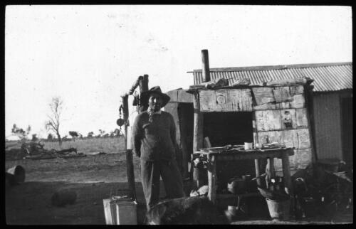 Man in front of bush dwelling [transparency] : part of scenes of the Northern Territory and North Western Australia / [John Flynn?]