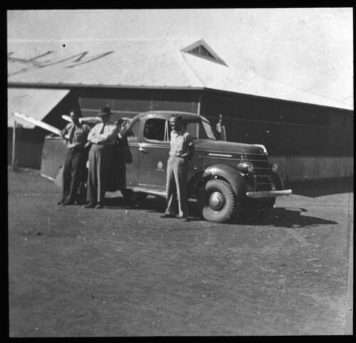 Three unidentified men standing next to a utility truck [transparency] : a lantern slide used for publicity in South Australia / [John Flynn]