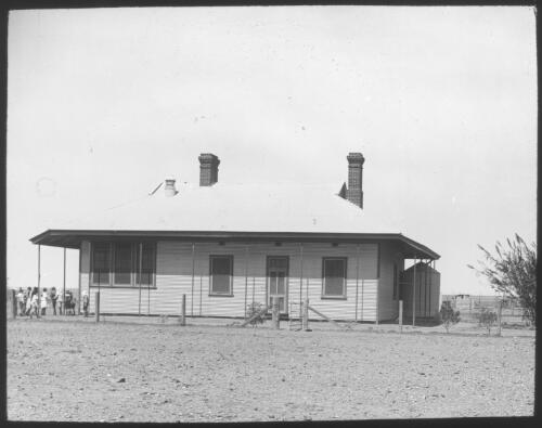Unidentified corrugated iron building with two chimneys and a group of children outside [transparency] / [John Flynn?]