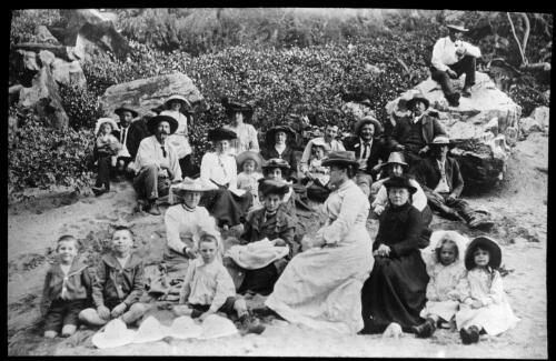 Group of unidentified people sitting on a river? bank [transparency] : part of a mixed selection of lantern slides and negatives from John Flynn's teaching days in Gippsland, and early AIM [Australian Inland Mission] activities/ John Flynn