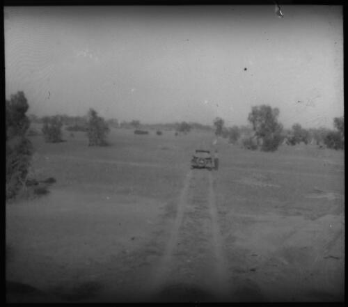 Unidentified man standing beside car on dirt track [transparency] / [John Flynn?]