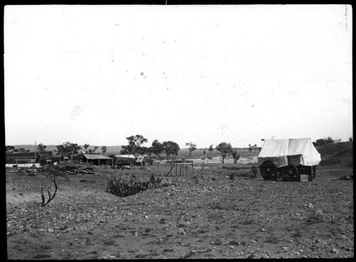 Covered wagon with buildings in background [transparency] : part of mixed selection of lantern slides and negatives from John Flynn's teaching days in Gippsland, and early AIM [Australian Inland Mission] activities / John Flynn