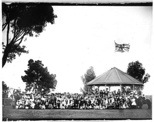 Empire Day celebrations?, group of people in front of a bandstand flying a Union Jack [transparency] : part of a mixed selection of lantern slides and negatives from John Flynn's teaching days in Gippsland, and early AIM [Australian Inland Mission] activities / John Flynn