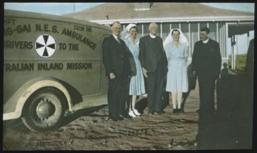 Three unidentified men and two nursing sisters standing next to an Australian Inland Mission ambulance [transparency] / [John Flynn?]