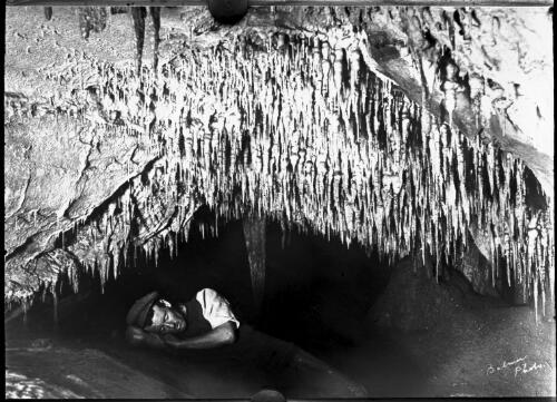 Frank Moon lying underneath some stalactites, Buchan Caves, Victoria [picture] : part of a mixed selection of lantern slides and negatives from John Flynn's teaching days in Gippsland, and early AIM [Australian Inland Mission] / John Flynn