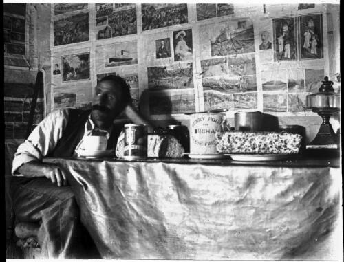 Unidentified man sitting at a table surrounded by Buchan, Victoria? memorabilia [picture] : part of a mixed selection of lantern slides and negatives from John Flynn's teaching days in Gippsland, and early AIM [Australian Inland Mission] / John Flynn