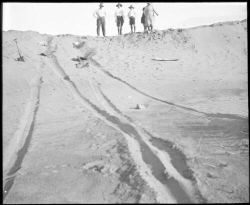Unidentified family looking down at tyre tracks in the sand [transparency] : taken during the Resonian trip to the Northern Territory led by John Flynn / [John Flynn?]