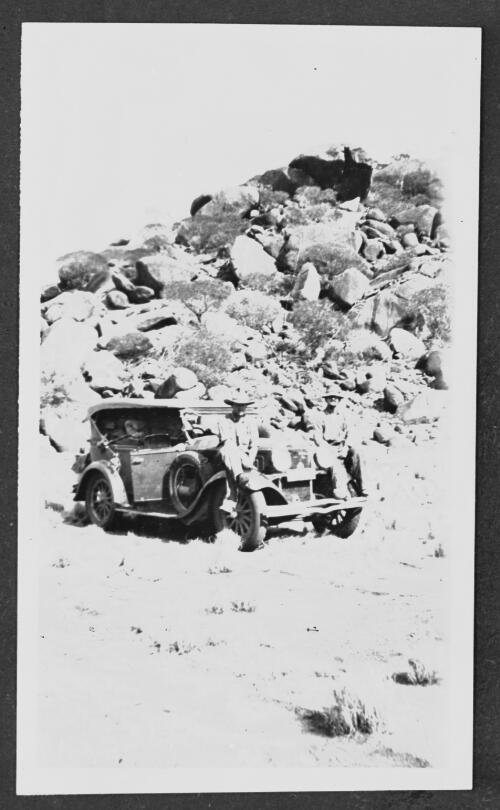 Two unidentified people sitting on the front of John Flynn's Dodge buckboard in the outback near a rocky hill [picture] / [John Flynn?]