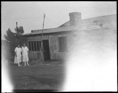 Two unidentified nurses? standing outside a corrugated iron building [transparency] : taken during the Resonian trip to the Northern Territory led by John Flynn / [John Flynn?]