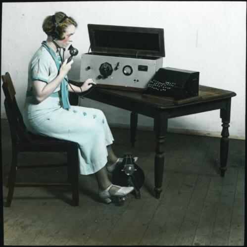 Unidentified woman with pedal powered transceiver and morse typewriter [transparency] : part of lantern slide lecture collection, 1926 / [John Flynn?]