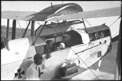 Side view of Pilot Eric Donaldson, Dr Allan Vickers, patient and wireless in the plane called Victory (DH50A) [transparency] : part of lantern slide lecture collection, 1926 / [John Flynn?]