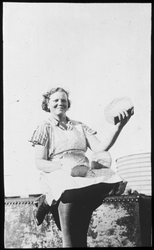 Portrait of an unidentified woman holding up a loaf of bread with two other loaves in her lap [transparency] : a lantern slide used in lectures on all Australian Inland Mission activities, [1940-]/ [John Flynn?]