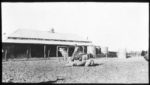 Two unidentified men on a camel in front of a homestead [transparency] : a lantern slide used in lectures on all Australian Inland Mission activities, [1940-]/ [John Flynn?]
