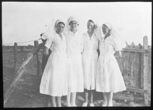 Portrait of four unidentified nurses standing next to a fence [transparency] : a lantern slide used by John Flynn in lectures / [John Flynn]