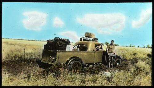 An unidentified man standing next to a bogged heavily laden Australian Inland Mission ute with an unidentified woman looking out the window [transparency] : a lantern slide used by John Flynn in lectures / [John Flynn]