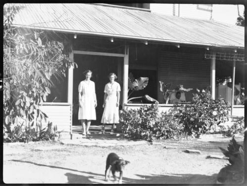 Two unidentified nursing sisters standing on the verandah of the Port Hedland hospital with a dog in the foreground [picture] : taken on a survey trip undertaken in 1927 by Rev. J.A. Barber and Dr. George Simpson for the Flying Doctor Scheme, Western Australia, 1927 ./ [J.A. Barber and George Simpson]