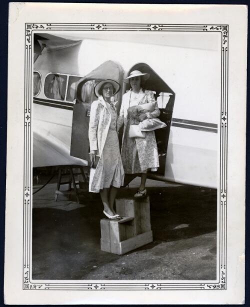 Two unidentified women posing in front of the plane they are about to board [picture] / [John Flynn?]