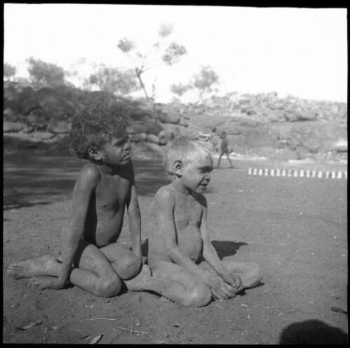 Two young boys seated on the ground at Ernabella Mission, South Australia, 1949 [transparency] / C. Duguid