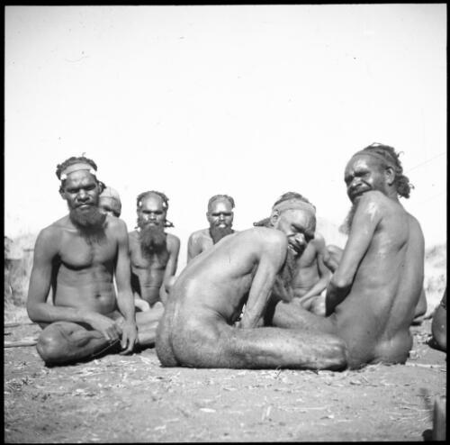 Man with scabeie [?] seated on the ground with a group of other men at Ernabella, South Australia, ca. 1946 [transparency] / C. Duguid