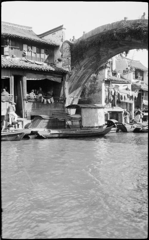 [Canal with bridge and barges alongside dwellings, China, ca. 1930] [picture] / Stanley O. Gregory