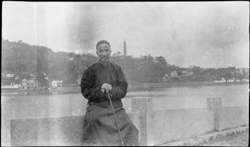 [Man with walking stick sitting on wall of West Lake Hangchow and Pao Shu pagoda in background, China, ca. 1930] [picture] / Stanley O. Gregory