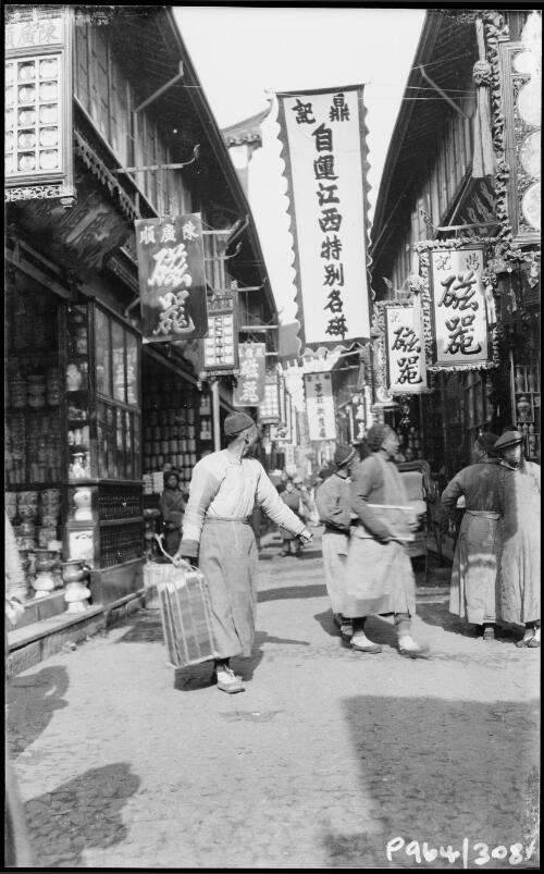 [Bannered street where person carrying a stack of papers tied with string looks over shoulder, China, ca. 1930] [picture] / Stanley O. Gregory