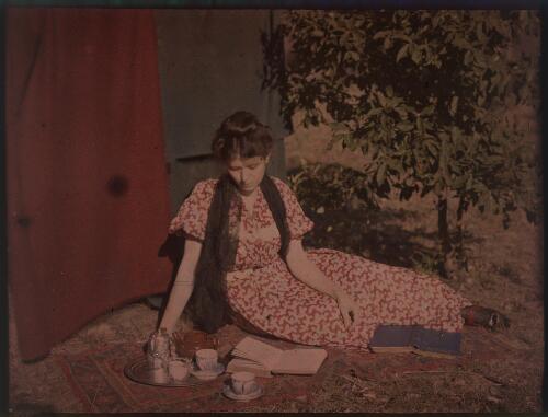 [Unidentified woman seated outdoors on a rug with tea set and books, ca. 1906] [transparency]